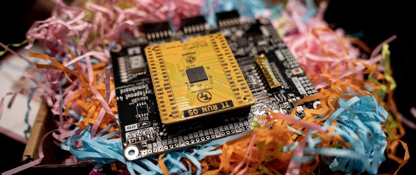 A Tiny Tapeout ASIC demoboard nestled in colourful shredded paper