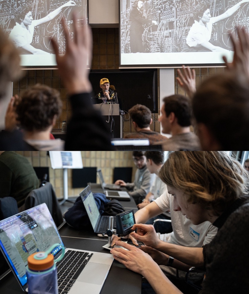 A packed lecture hall of workshop attendees with hands raised